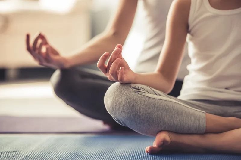 The core - Two females wearing gym clothes sat cross-legged on mats in a studio adopting the lotus position in yoga