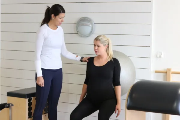 A pilates instructor - Two females, one pregnant, in a pilates studio.