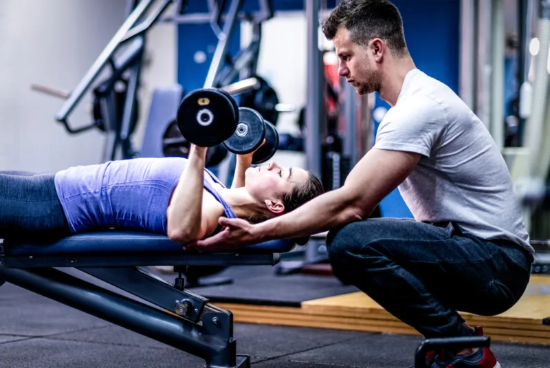 Why women need strength training - A young woman being guided in correcting her posture for weight training