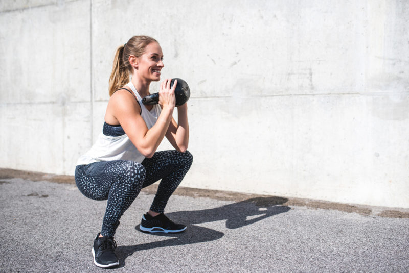 Mobility Vs Flexibility - Woman practising squats using a kettle bell outside