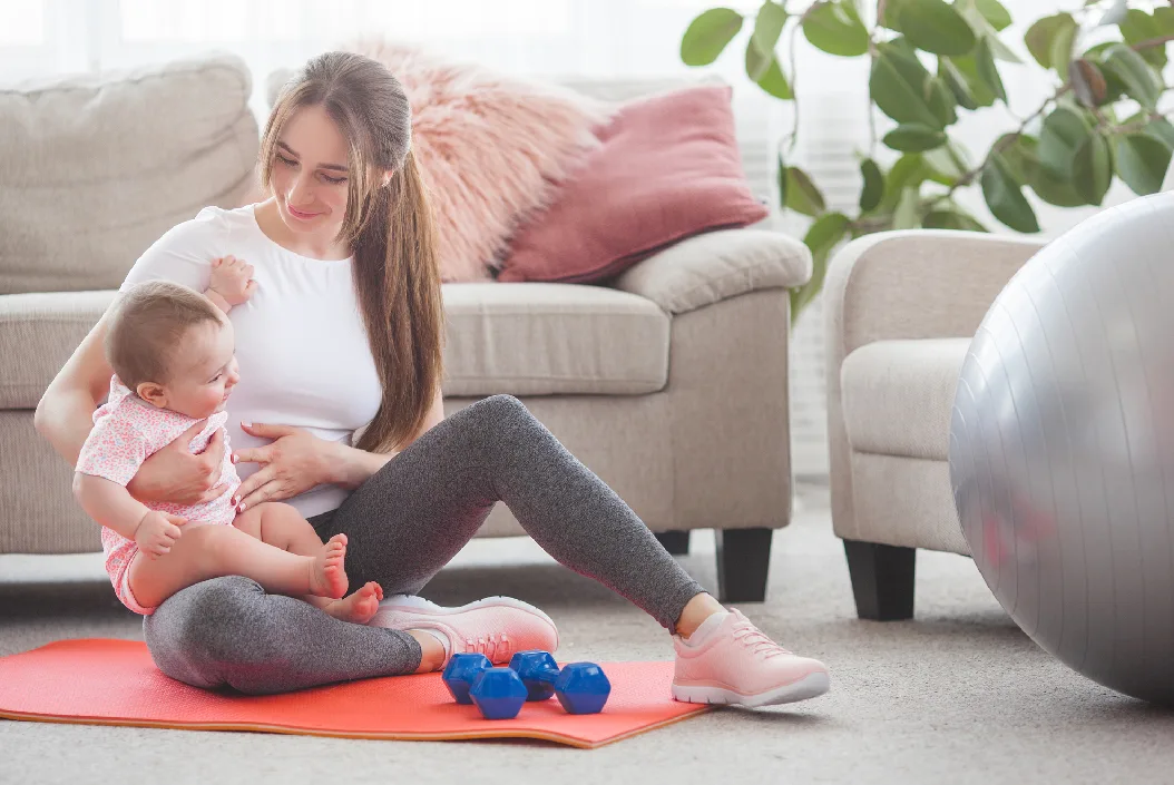 postnatal depression - A young mother with baby in her lap sitting on the floor of a lounge with play equipment