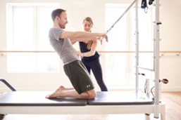 Pilates and chronic lower back pain - A female Pilates instructor assisting a man in his Pilates move using a machine in a studio.