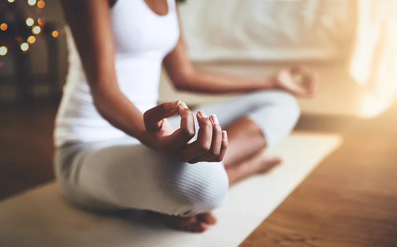 Pilates Principles - Breathing - A slim woman sitting cross-legged on a mat with her wrists on her knees, palms upward with the thumb and forefinger touching