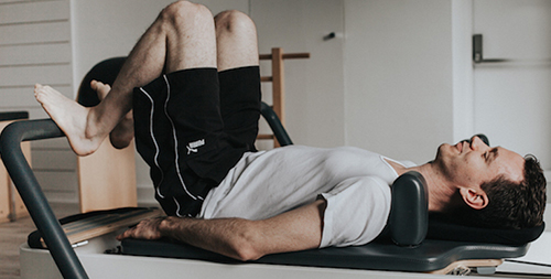 Pilates for men - A white male performing Pilates exercise with the guidance of a pilates instructor