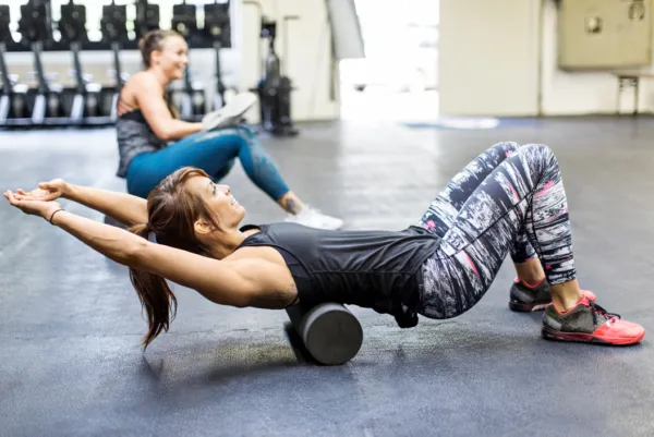 foam rolling - a woman in a gym laying on the floor foam rolling her upper back