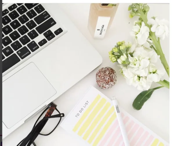 A pilates instructor - An overhead shot of an office desk showing a section of a laptop, notepad and pen, spectacles, a sprig of flowers and a ball of protein