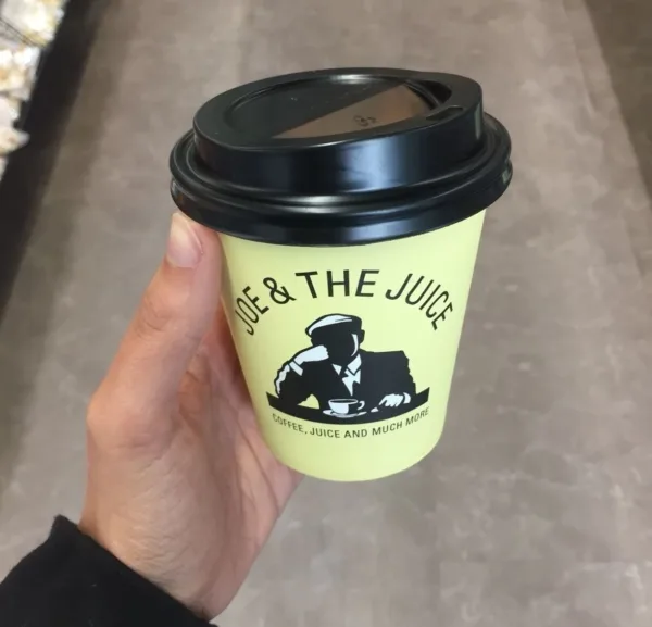 A pilates instructor - hand holding a yellow takeaway coffee cup with black plastic lid