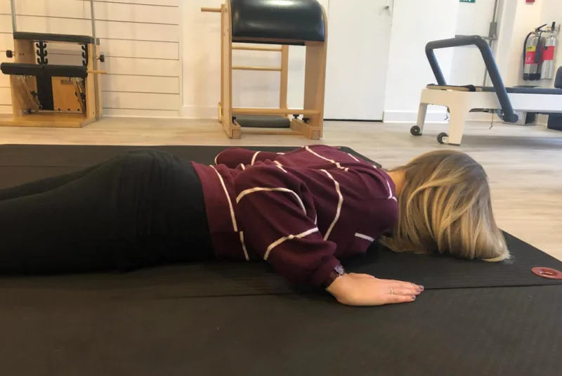 Pilates Swan - A female lying face down on a gym mat.