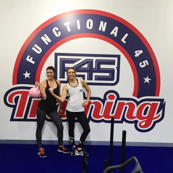 A pilates instructor - Two females standing in front of a wall with a large painted sign