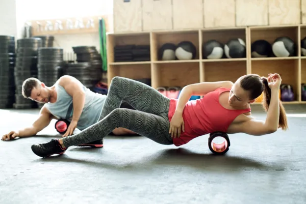 foam rolling - male and female foam rolling their shoulders on the floor of a gym