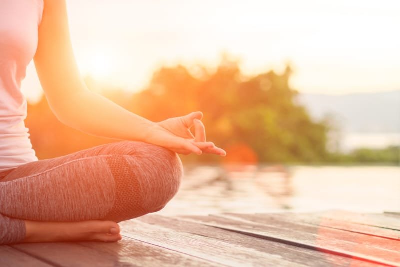 Yoga advantages - A woman meditating on a pontoon by a lake at sunrise